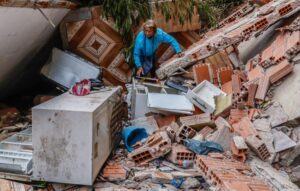Uma pessoa está no meio de escombros de uma casa destruída pelas chuvas